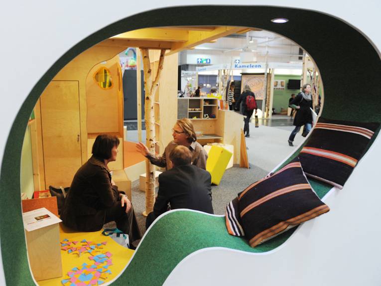 Sitzende Menschen im Gespräch durch eine Öffnung in einer Wand gesehen.