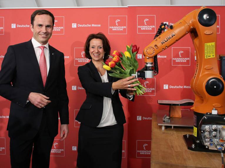 Ein Mann und eine Frau mit Industrieroboter und Blumenstrauß