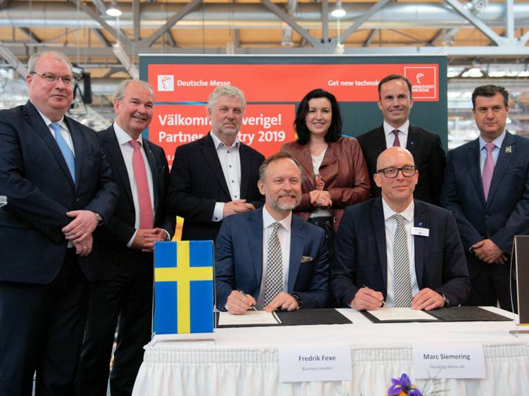 Menschen an einem Tisch mit schwedischer und deutscher Fahne stehend und sitzen 