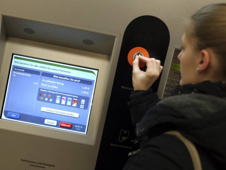 Frau steckt Münze in einen Fahrkartenautomaten
