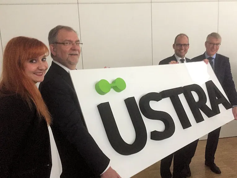 Eine Frau und drei Männer präsentieren den Schriftzug "üstra"