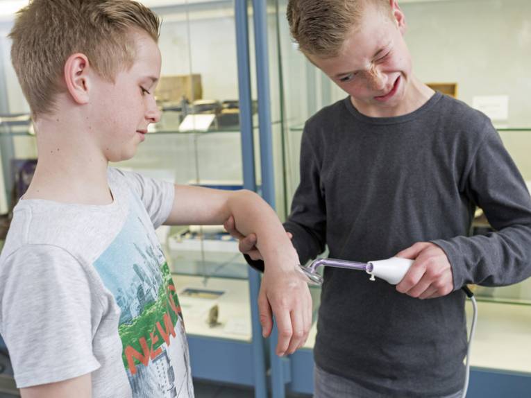 Eine Junge hält einem anderen eine elektrisches Gerät an den Arm.