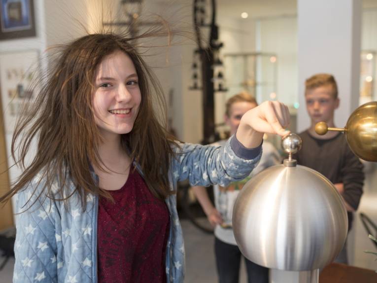 Einem Mädchen stehen bei einem elektrischen Experiment die Haare zu Berge