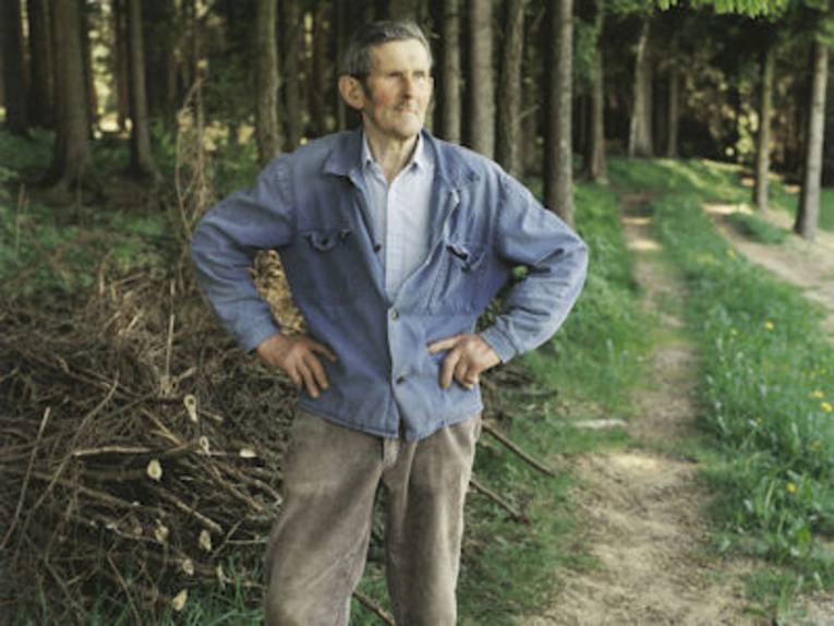 Portrait alter Mann in Arbeitskleidung vor einem Waldstück