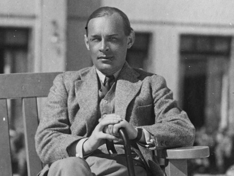 Schwarzweiß-Foto eines Mannes im Anzug mit Spazierstock, der auf einer Bank sitzt.