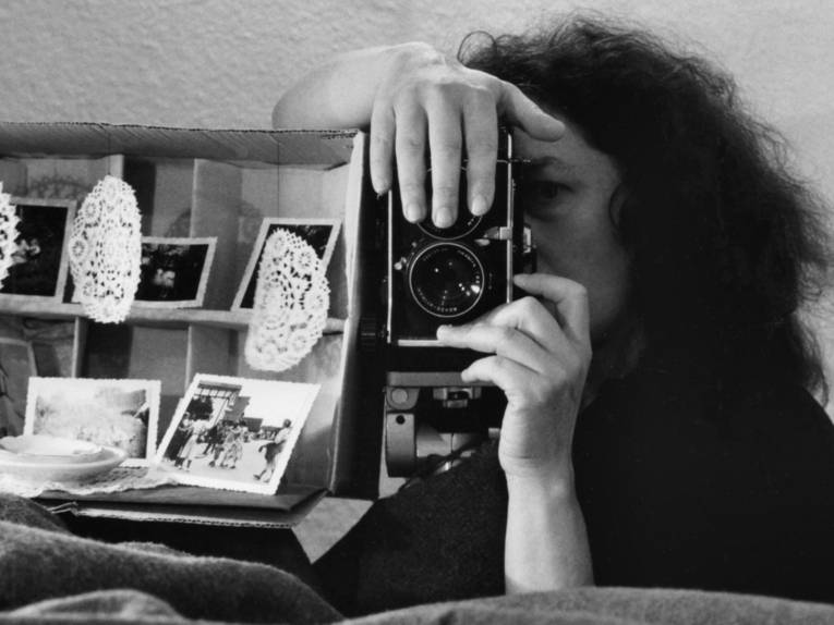 Schwarzweißfoto, das eine Frau zeigt, die durch den Sucher eines Fotoapparates schaut.