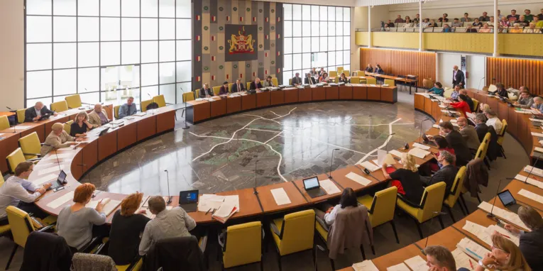 Saal mit elipsenförmig angebrachtem Tisch, an dem Menschen sitzen
