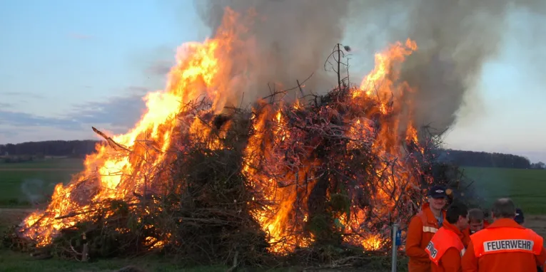 Feuerwehrmänner und Menschen vor einem lodernden Osterfeuer