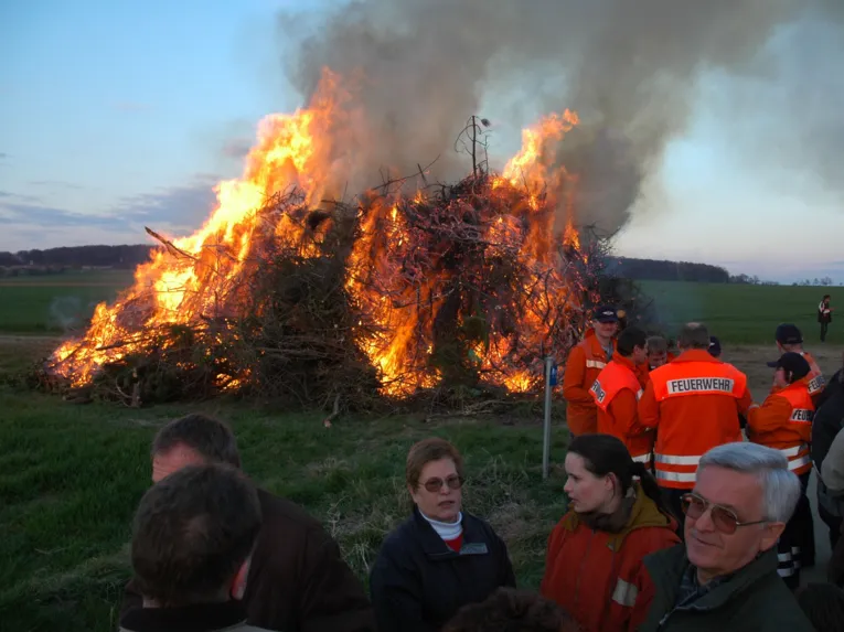 Feuerwehrmänner und Menschen vor einem lodernden Osterfeuer