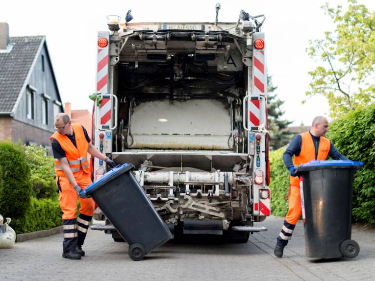 Zwei Müllmänner mit Mülltonnen hinter Müllauto