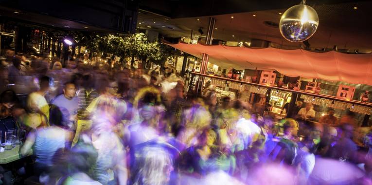 Viele tanzende Menschen in einem Raum vor einer Bar. 