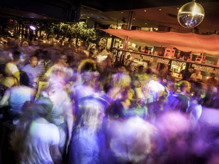 Viele tanzende Menschen in einem Raum vor einer Bar. 