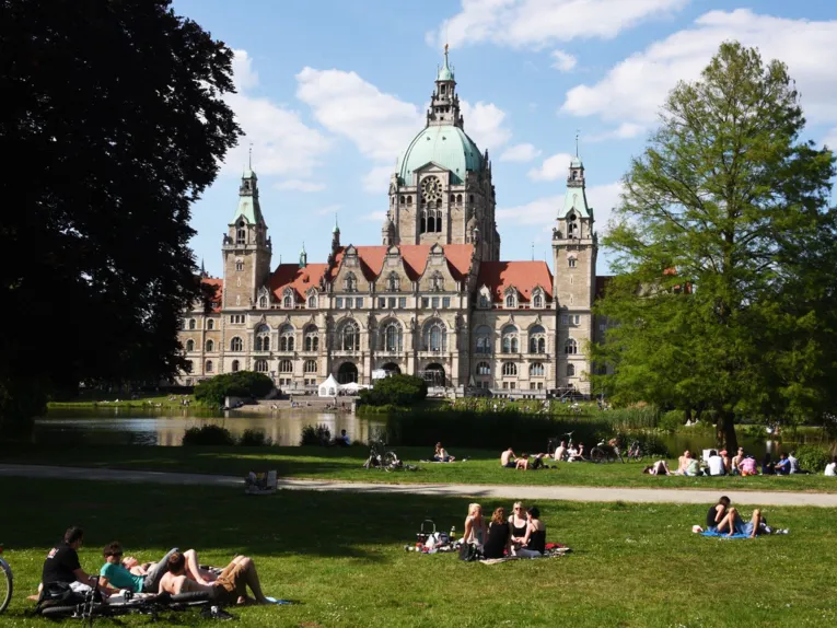 Menschen auf einer Wiese um ein Rathaus.