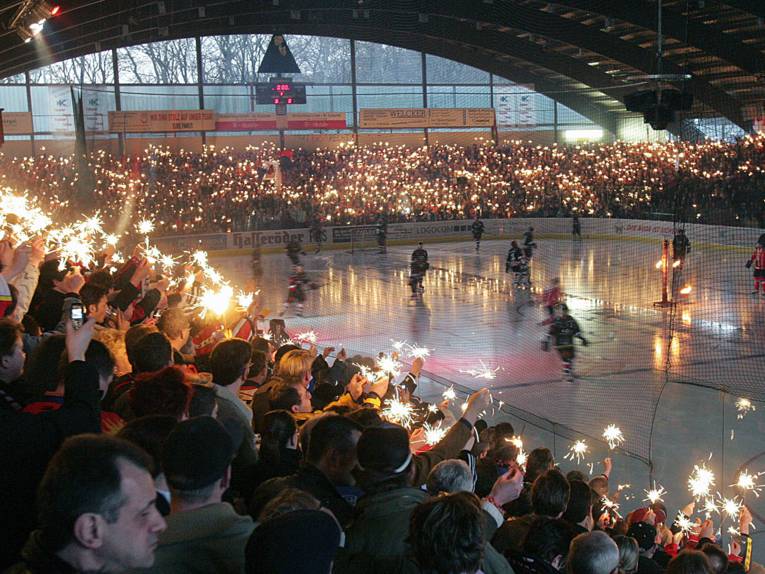 Menschen mit Wunderkerzen in den Händen in einem Eishockeystadion.