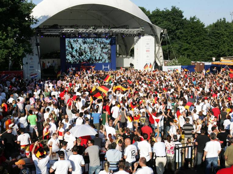 Menschenmenge mit Deutschlandfahnen vor Großbildleinwand.