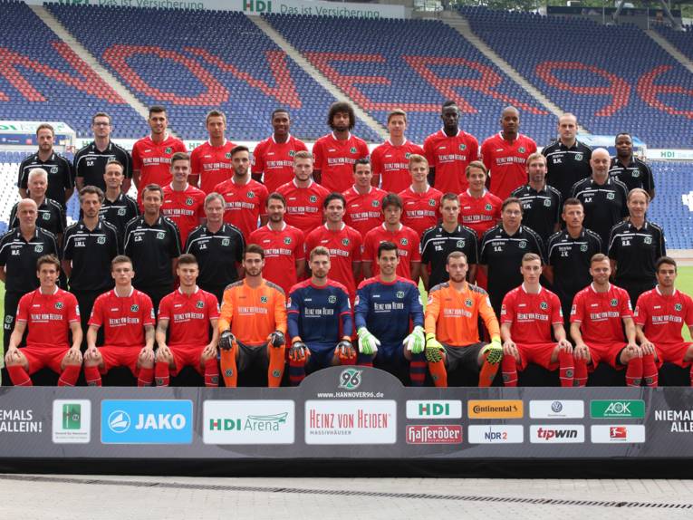 Spieler, Trainer und Betreuer einer Fußballmannschaft in vier Reihen hintereinander in einem Stadion.