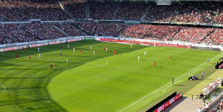 Blick in gefülltes Stadion mit Fußballspielern auf dem Feld