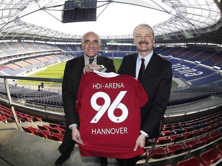 Zwei Männer stehen in einer Arena und halten ein Fußballtrikot in den Händen.