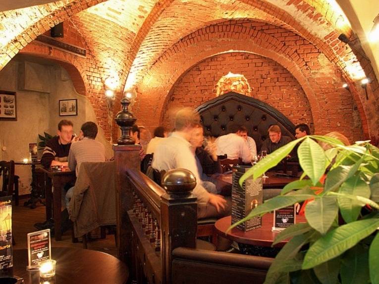 Menschen sitzen an Tischen in einem Raum mit Kreuzgewölbe.