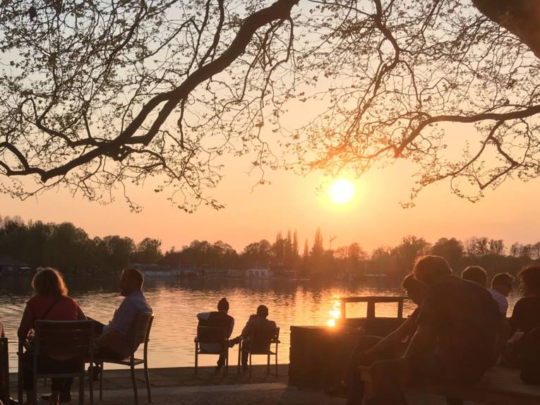 Leute sitzen bei Sonnenuntergang an einem See