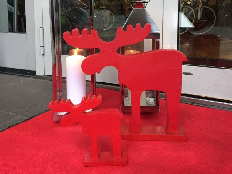 Rote Elchfigur und weiße Kerze auf rotem Teppich vor einem Geschäftseingang.