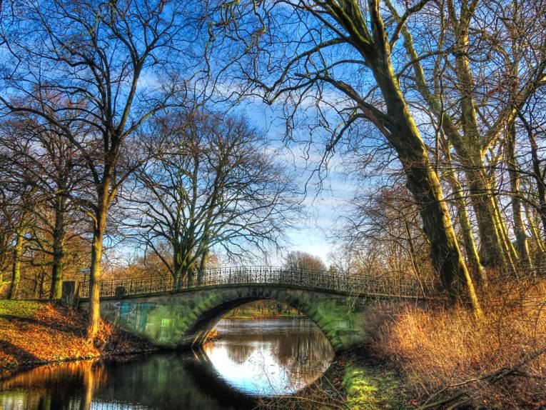 Brücke über Gewässer in einer Parklandschaft im Winter ohne Schnee
