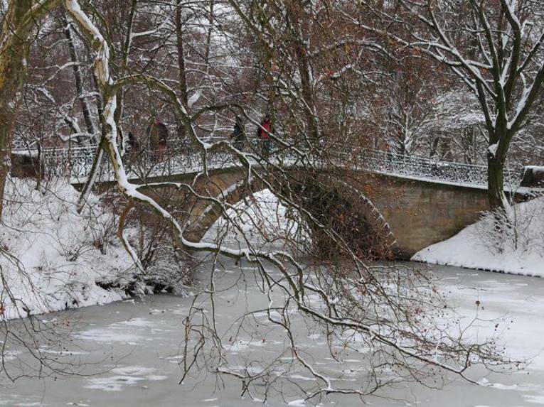 Ein zugfrorener Flußlauf, eine kleine Brücke und verschneite Bäume.
