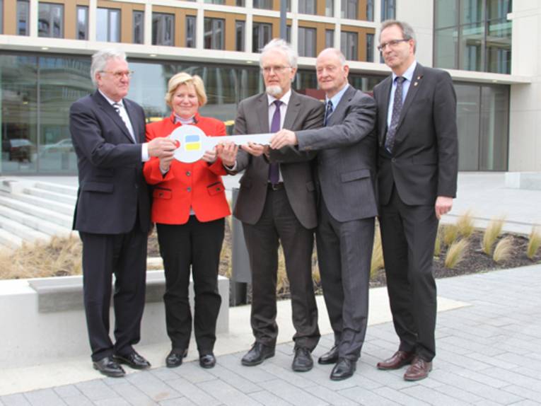 Vier Männer und eine Frau halten einen überdimensionerten Schlüssel in der Hand.