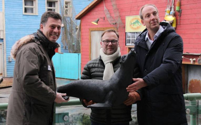 Drei Männer präsentieren eine Skulptur in Form eines Seelöwen