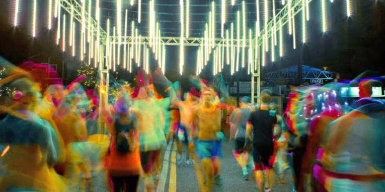 Mit bunten Leuchtmitteln behangene Läufer auf einem beleuchteten Parcours.