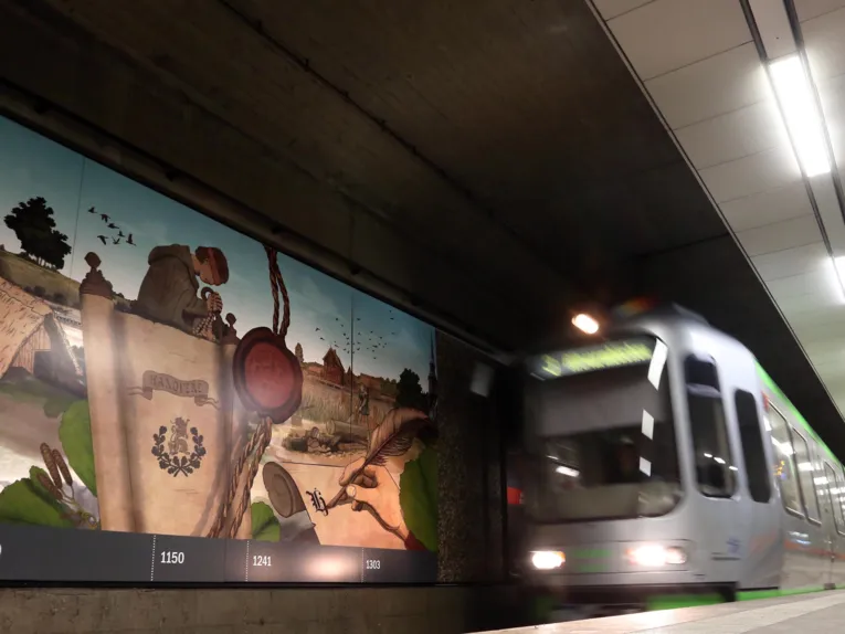 Eine Bild-College an der Wand eines Stadtbahn-Gleises und eine einfahrende Stadtbahn.