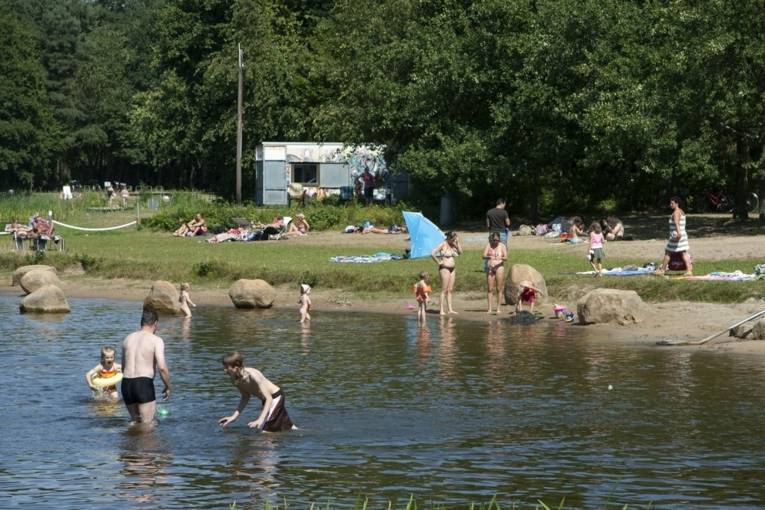 Jugendliche und Kinder spielen in der Flachwasserzone eines Sees, im Hintergrund Menschen, die sich sonnen oder am Ufer entlang spazieren