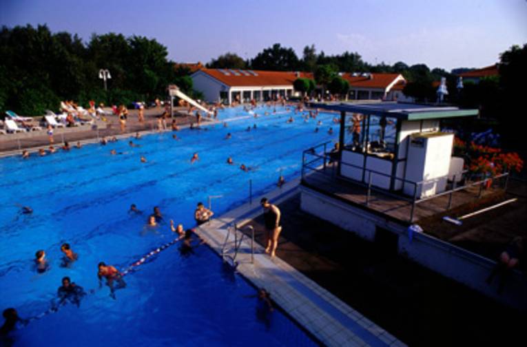 ein Schwimmbecken mit Abtrennung zwischen Schwimm- und Sprungbereich, im Hintergrund weisse Gebäude mit roten Dächern