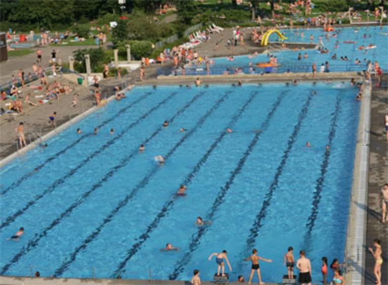 Zwei Schwimmbecken, schwimmende Menschen, im Hintergrund eine gelbe Rutsche