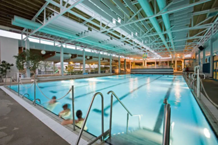 Blick auf das fast leere, beleuchtete Schwimmerbecken, drei Badende lehnen sich gegen den Beckenrand