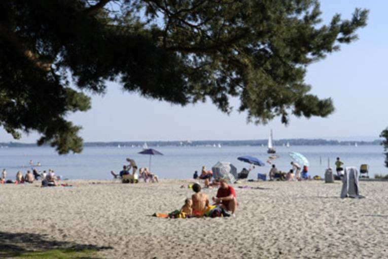 Ein Strand mit einigen Strandgästen in Badeanzügen, im Hintergrund Segelschiffe auf dem Steinhuder Meer.