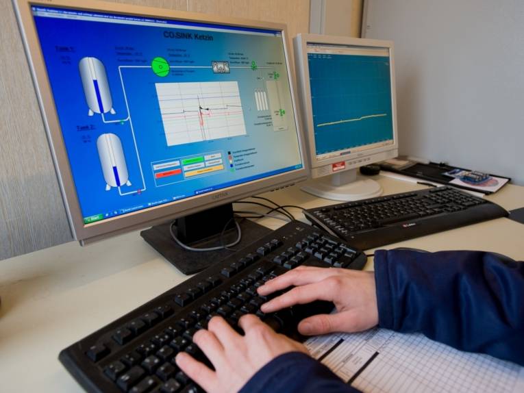 Hände auf einer Tastatur vor einem PC Monitor 