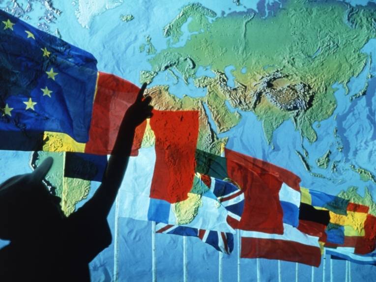 In einer Reihe wehende Flaggen von EU Mitgliedsstaaten vor einem geografischen Auschnitt von Europa