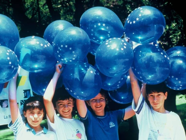 Kinder halten blaue Ballons mit weißen Sternen bedruckt in die Luft