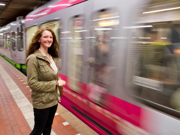 Junge Frau steht in einer U-Bahnstation und eine Bahn fährt ein.