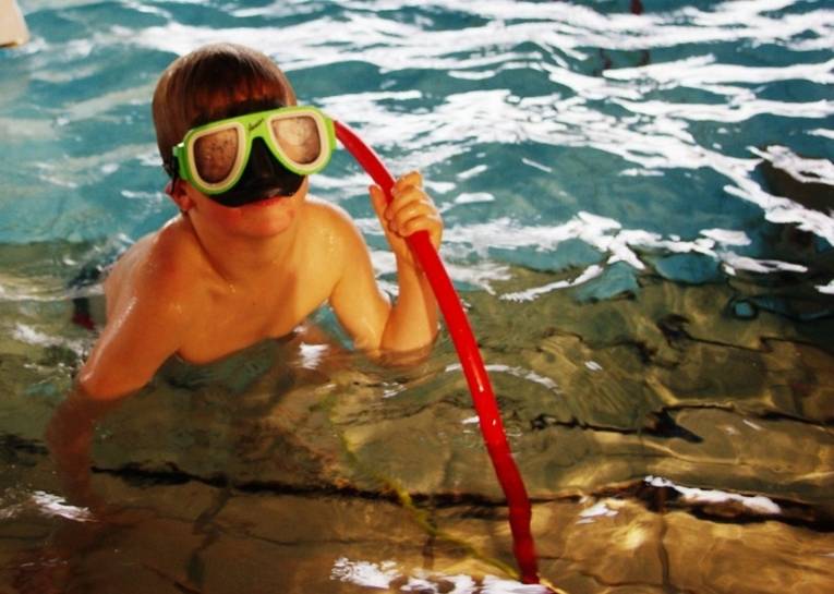 Junge mit Taucherbrille und rotter Plastikstange im Hallenbad
