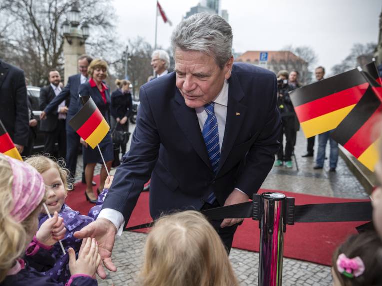 Bundespräsident Gauck beugt sich vor dem Neuen Rathaus zu einer Gruppe Kinder herab und schüttelt deren Hände