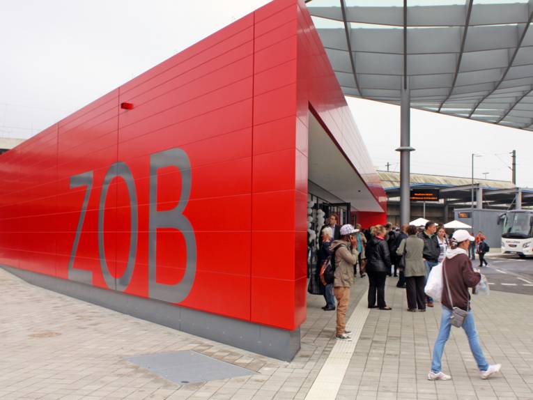 Blick auf das rote Servicecenter des neuen ZOB, vor dem Eingang stehen einige Dutzend Personen