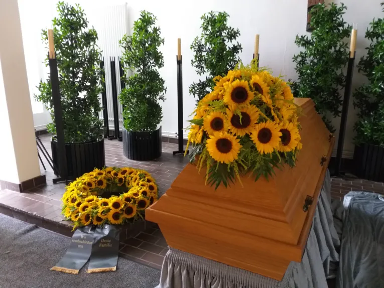 Blumenschmuck auf und neben einem Sarg.