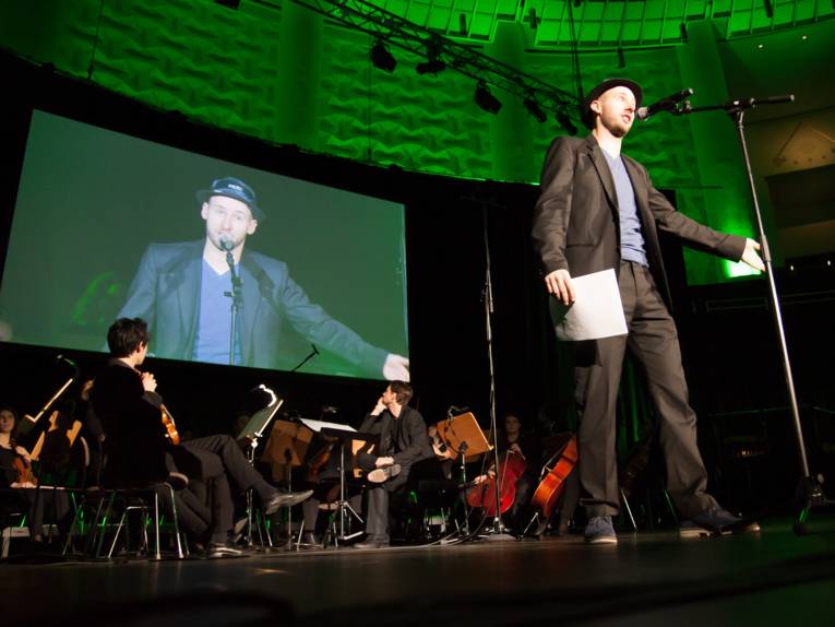 Ein Mann steht auf einer Bühne und spricht in ein Mikrofon.