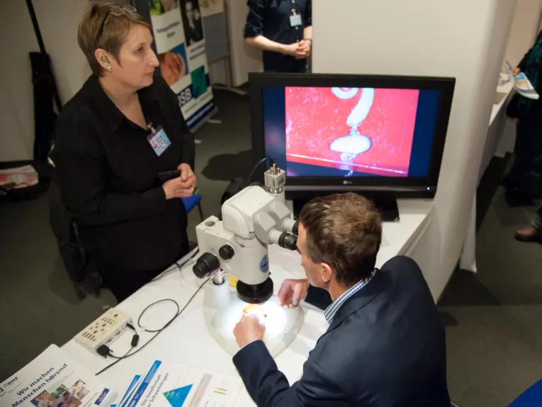 Ein Mann schaut an einem Informationsstand durch ein Mikroskop, eine Frau steht hinter dem Stand.