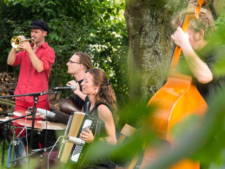 Eine Musikerin und drei Musiker mit Instrumenten im Garten.