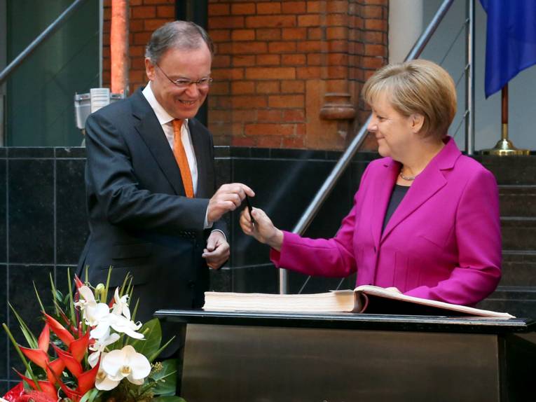 Angela Merkel gibt bei der Eintragung ins Goldene Buch den Stift an Stephan Weil weiter