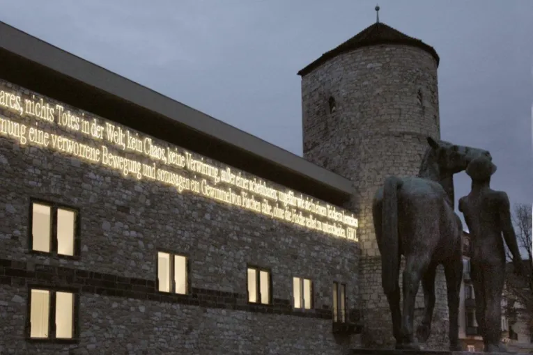 Schriftzug in Lichtröhren an einem alten Gemäuer.