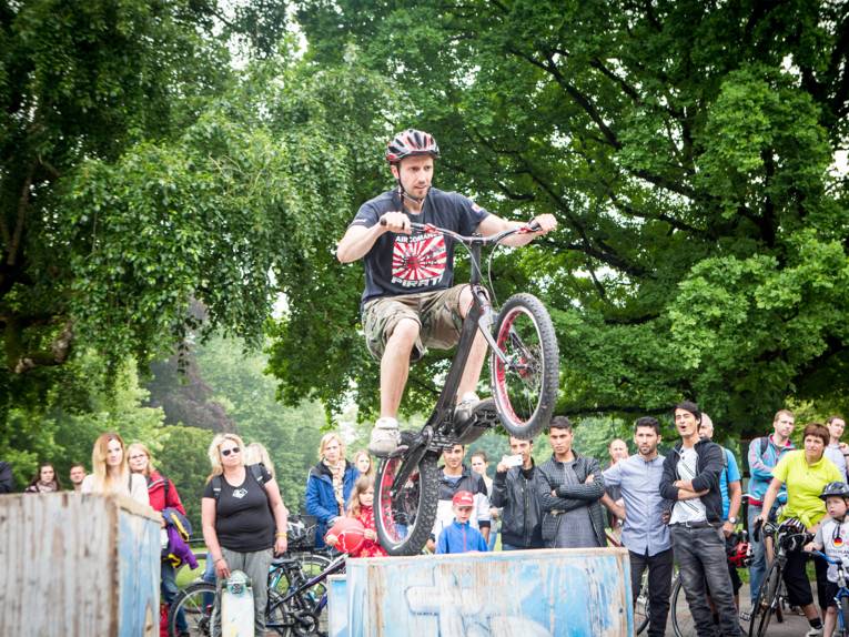 Junger Mann zeigt vor Publikum, wie gut er sein BMX-Fahrrad auch halb in der Luft beherrscht